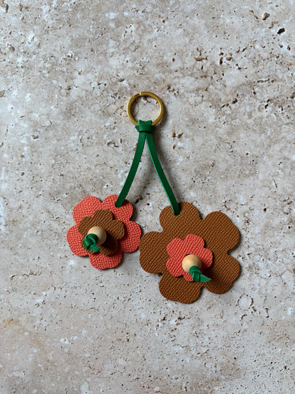 le porte clefs en cuir en forme de fleur corail et marron est présenté à plat sur un fond en travertin. 