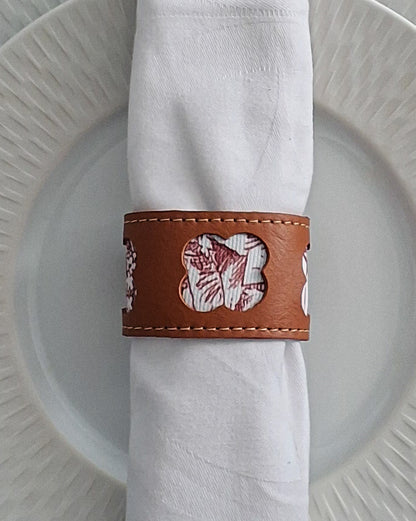 Serviette blanche roulée maintenue par un rond de serviette en cuir marron avec motif embossé disposé sur une assiette.