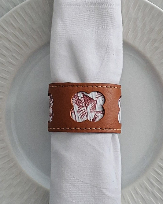 Serviette blanche roulée maintenue par un rond de serviette en cuir marron avec motif embossé disposé sur une assiette.