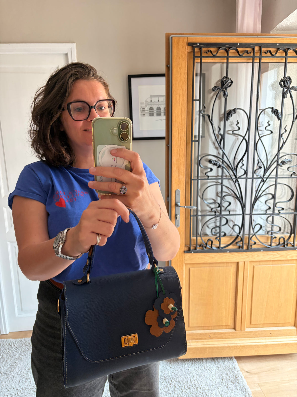 le sac Simone en cuir bleu est présenté porté par un modèle qui le tien à la main devant un miroir baroque