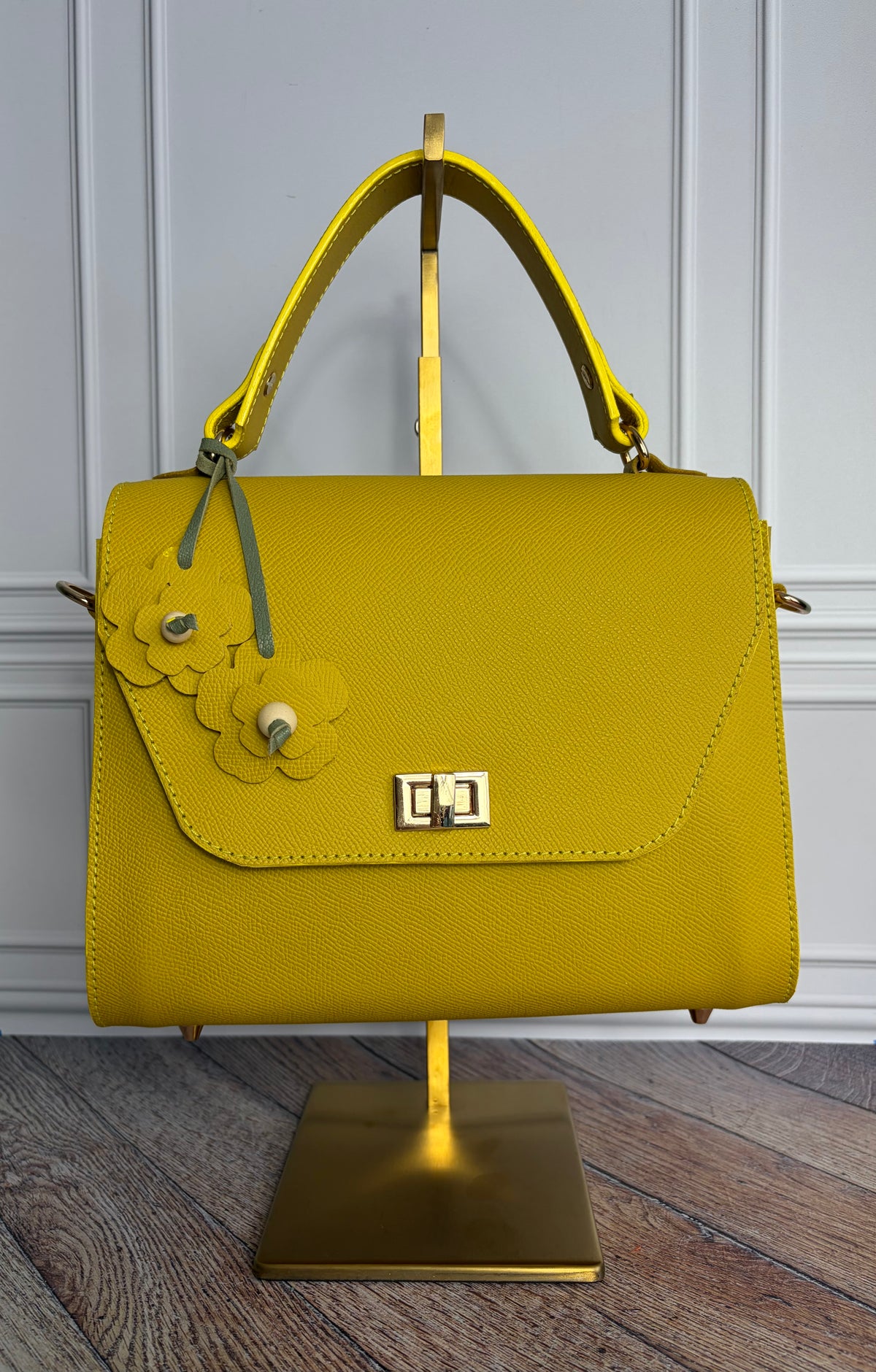 Le sac Simone en cuir jaune est présenté sur un support de sac en laiton de face. 