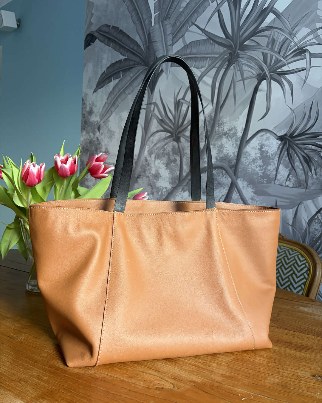 photo du sac cabas Albane en cuir marron au tannage végétal et anses en cuir noir posé sur une table en bois avec un bouquet de tulipe derrière. 