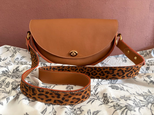 le sac demi lune en cuir grainé marron est présenté de face avec la sangle bi couleur devant. 