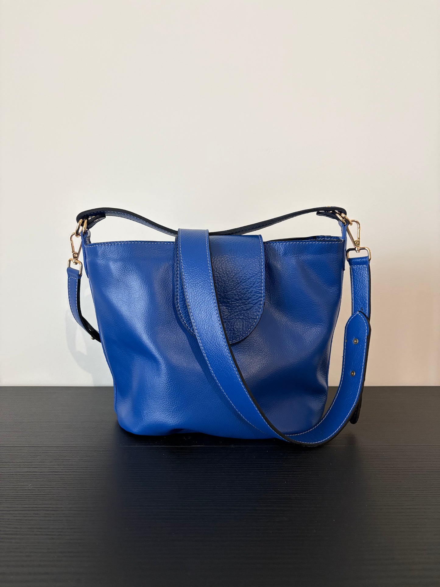 le sac garance bleu est posé sur une table en bois noire devant un mur blanc