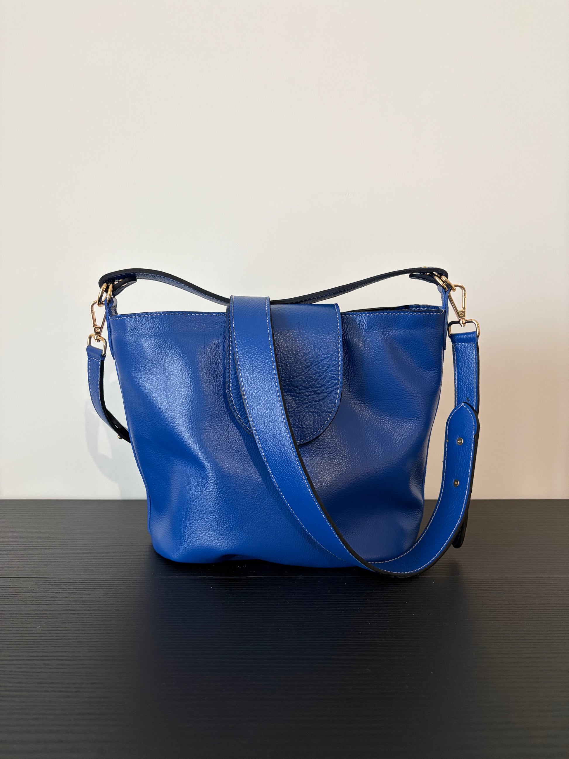 le sac garance bleu est posé sur une table en bois noire devant un mur blanc