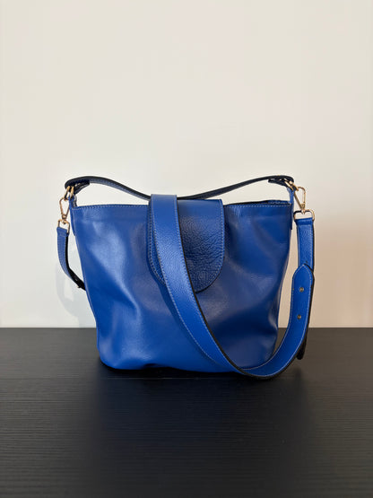 le sac garance bleu est posé sur une table en bois noire devant un mur blanc