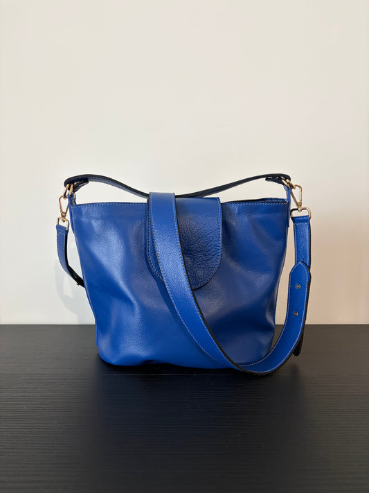 le sac garance bleu est posé sur une table en bois noire devant un mur blanc