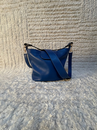 photo du sac seau Garance en cuir bleu grande taille posé sur un tapis beige texturé. 
