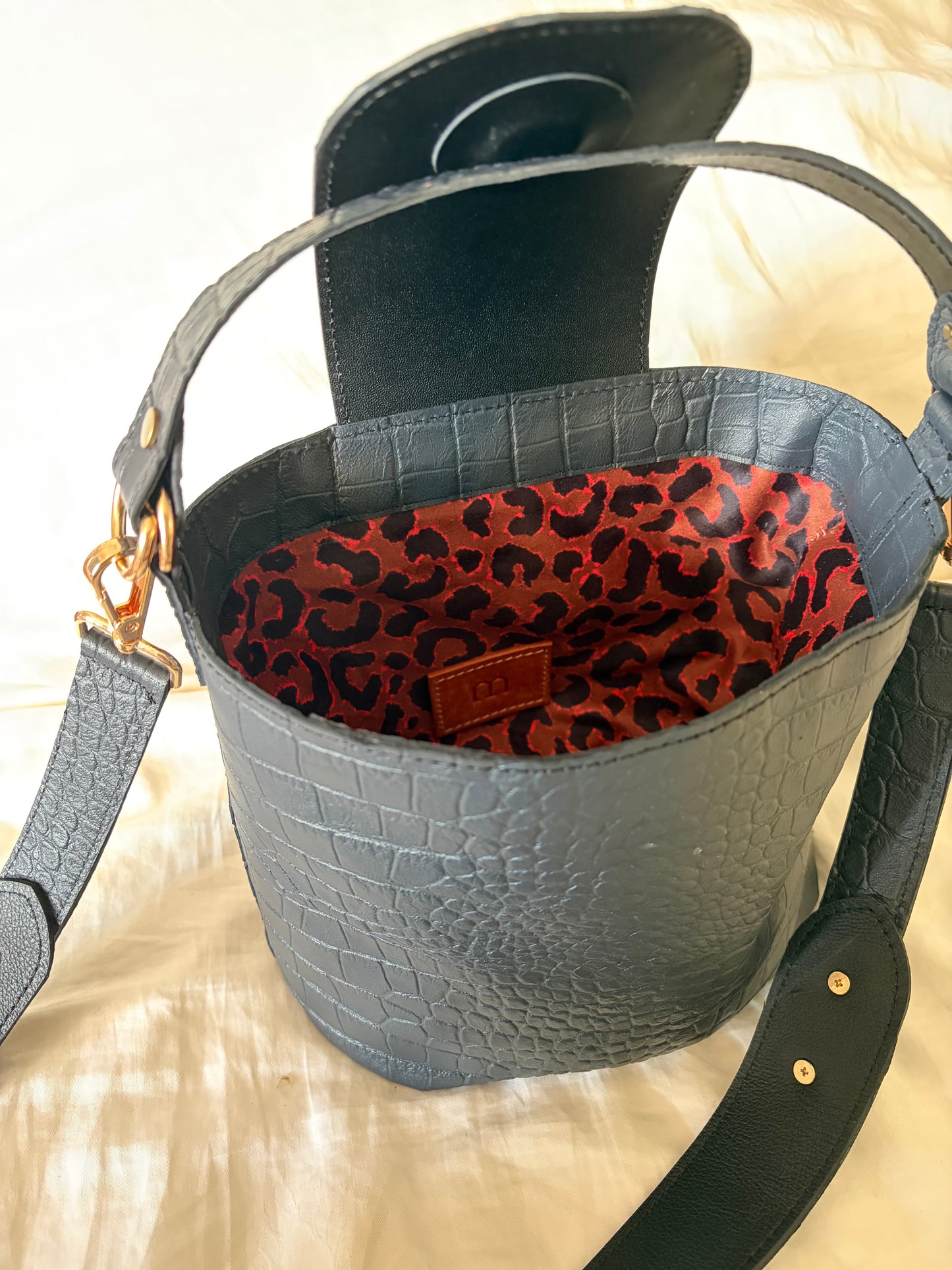 sac à main en cuir noir aspect crocodile posé sur un tissu avec une doublure motif léopard visible 