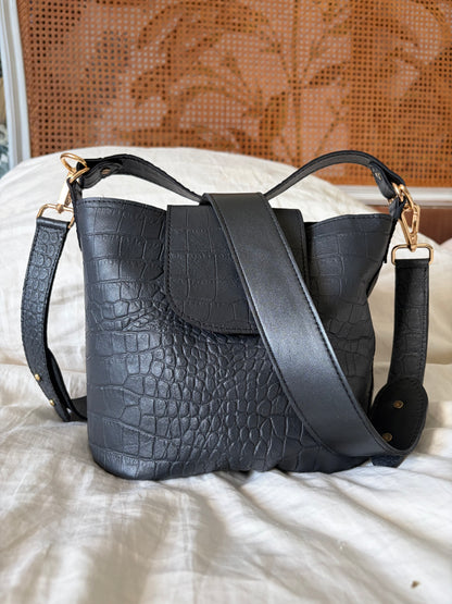 sac à main en cuir noir matricé crocodile posé sur un lit 