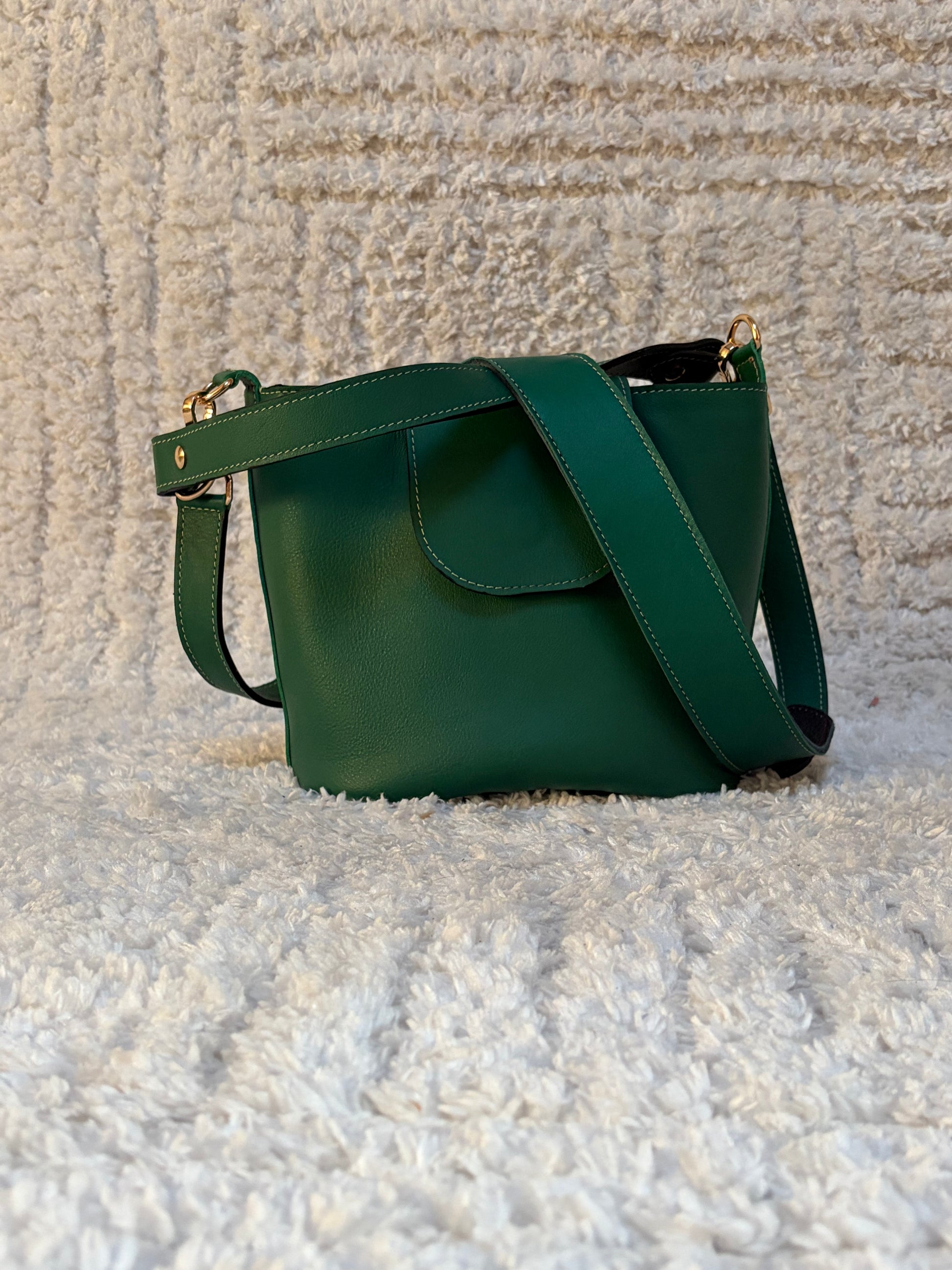 le sac seau garance en cuir vert est posé sur un fond laineux blanc