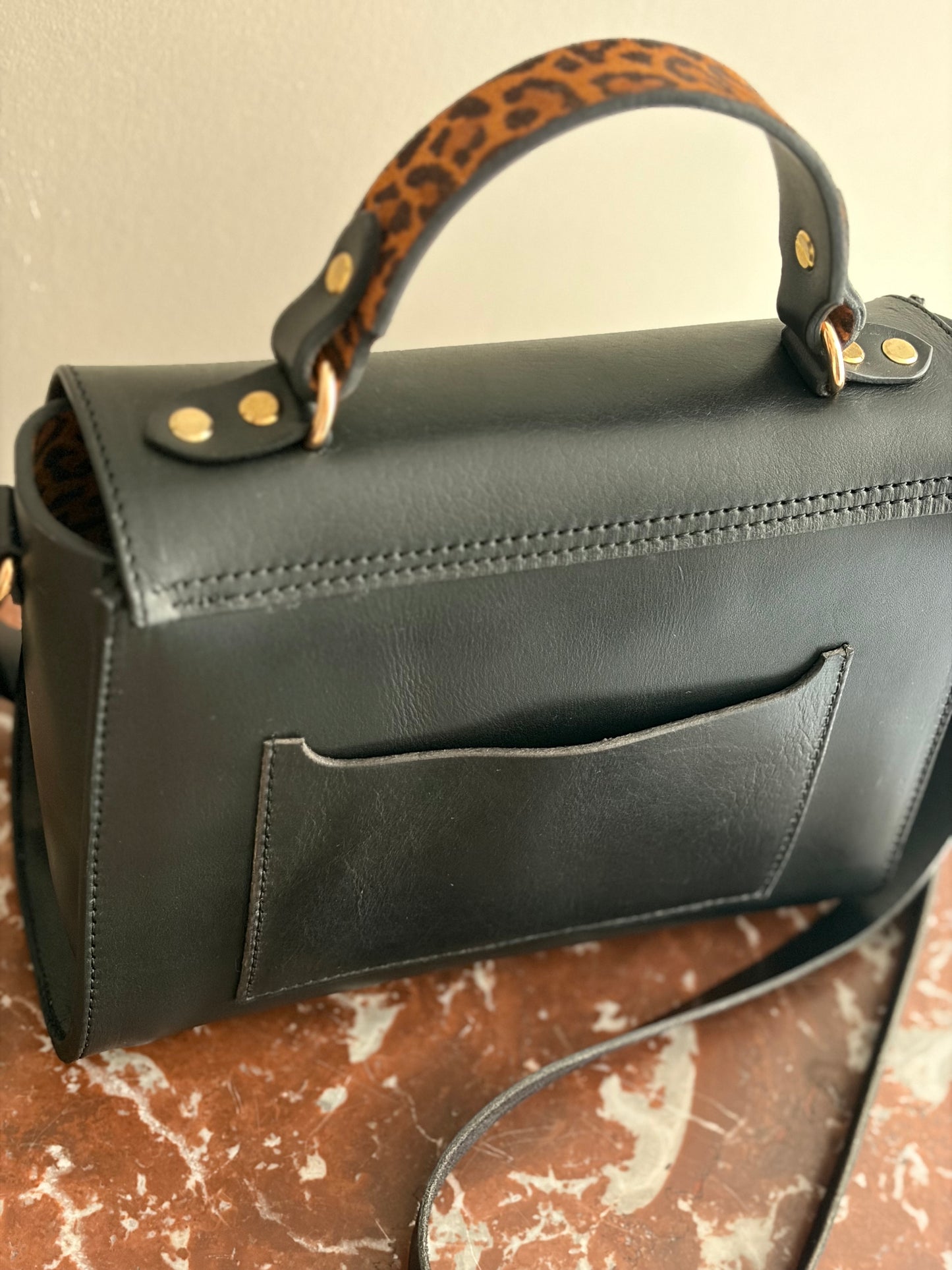 le sac est présenté de dos sur une table avec un dessus en marbre rouge