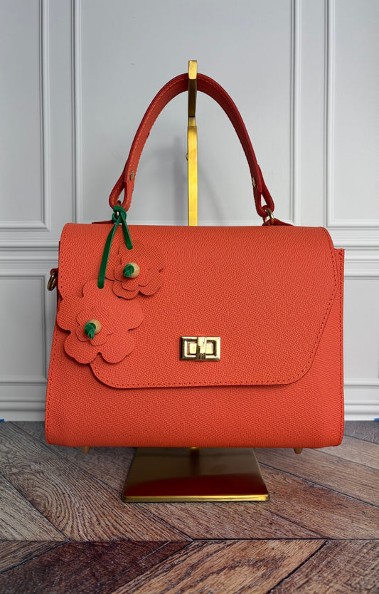 Le sac Simone en cuir corail est présenté sur un support de sac en laiton de face. 