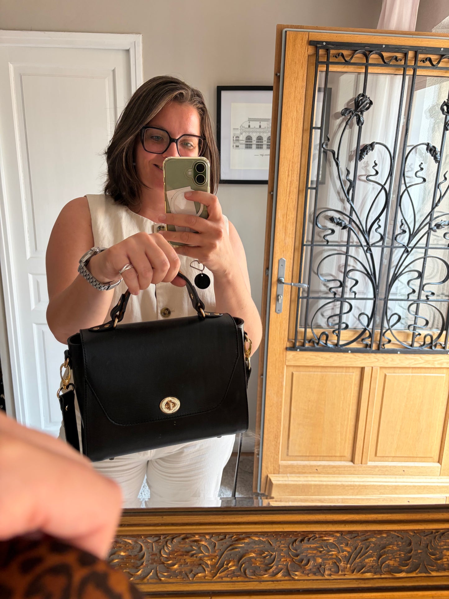 le sac simone est porté par un mannequin dans un décors d'entrée de maison bourgeoise. le sac est porté à la main et est mis en avant 