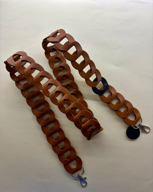 la sangle à portable en maillons de cuir marron est déposé sur un fond blanc