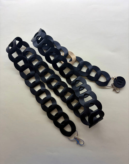 la sangle à portable en maillons de cuir noir est posée sur un fond blanc