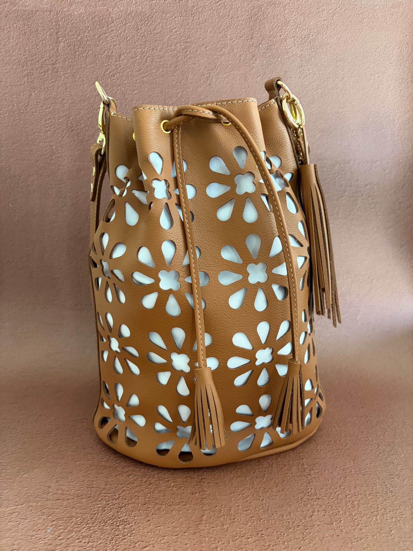 vue d'ensemble du sac sur un fond ocre. le détail des perforations en broderie anglaise est bien mis en avant. les pompons de bout de cordon sont également bien visible. 